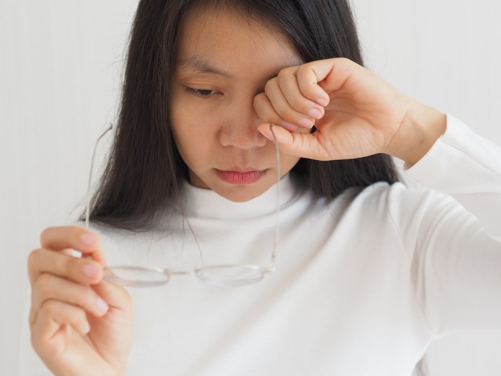 Young asian woman rubbing her eye to clear her vision after seeing eye floaters, perhaps in need of laser vitreolysis.