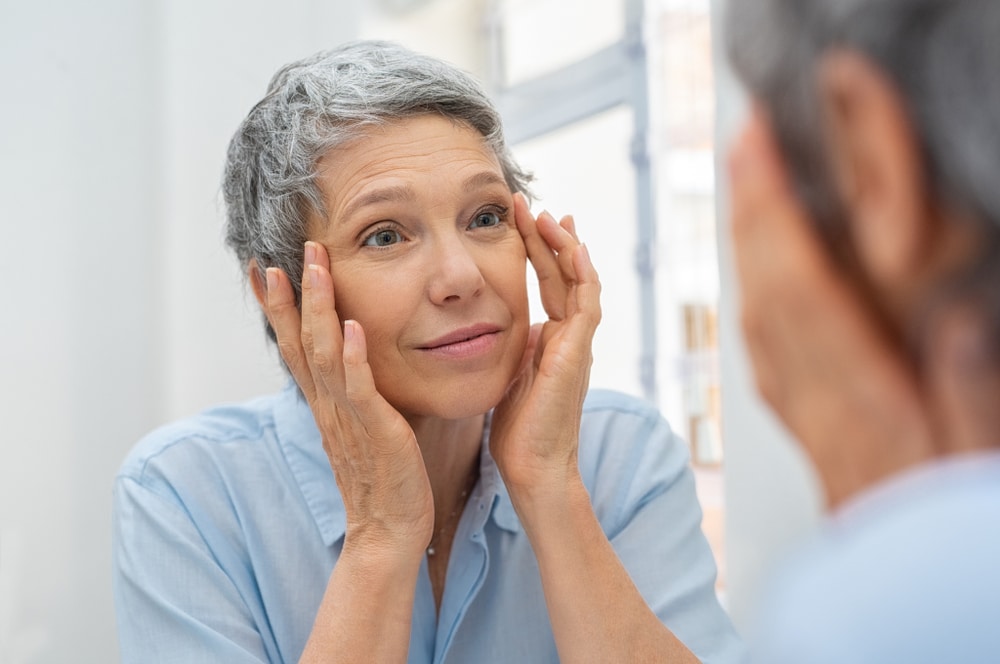 An older woman looking at her eyes in the mirror, not needing glasses after her refractive lens exchange.